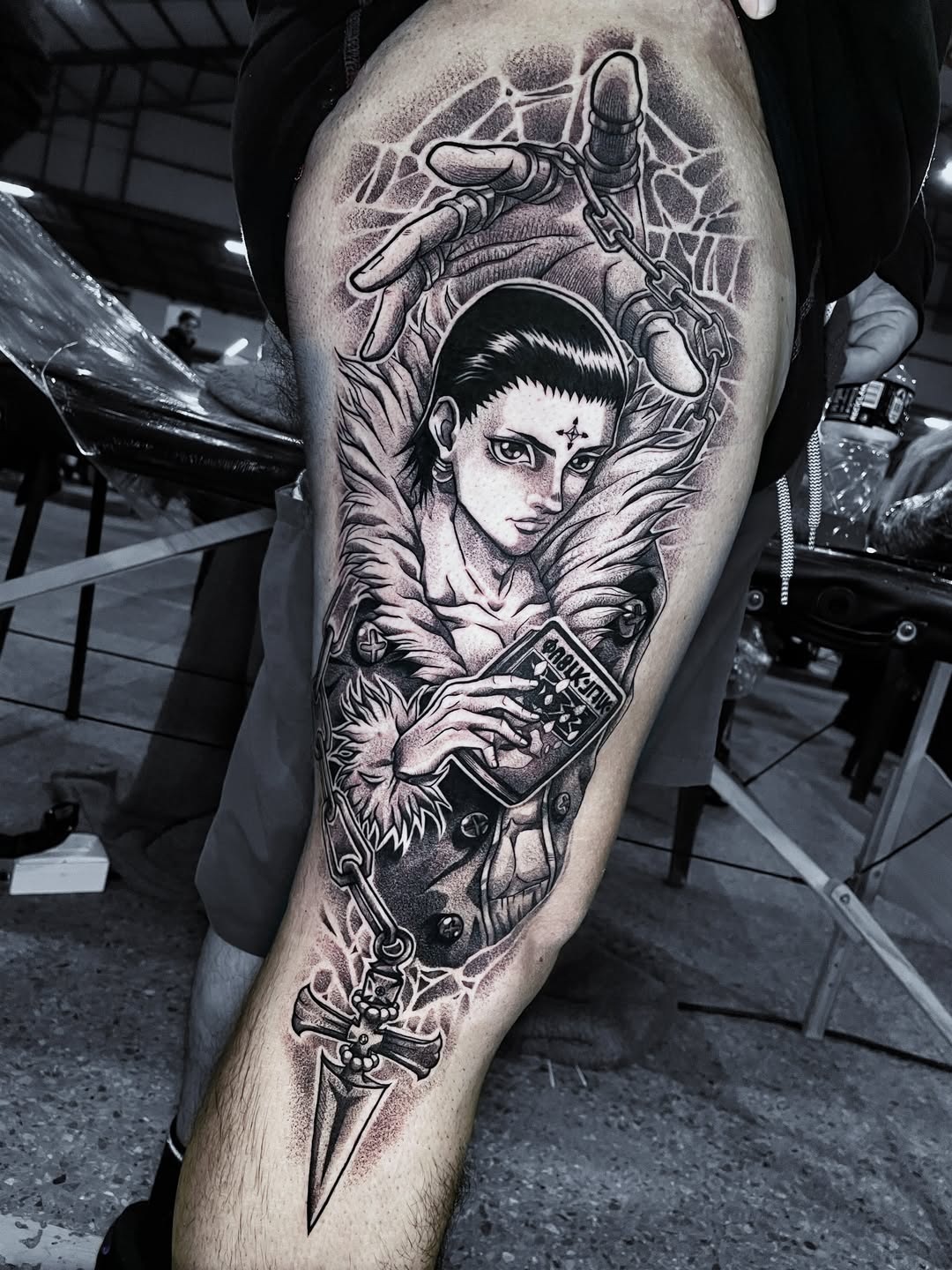 Tatuaje de Chrollo Lucilfer de Hunter x Hunter en el muslo, con telaraña y cruz en blackwork