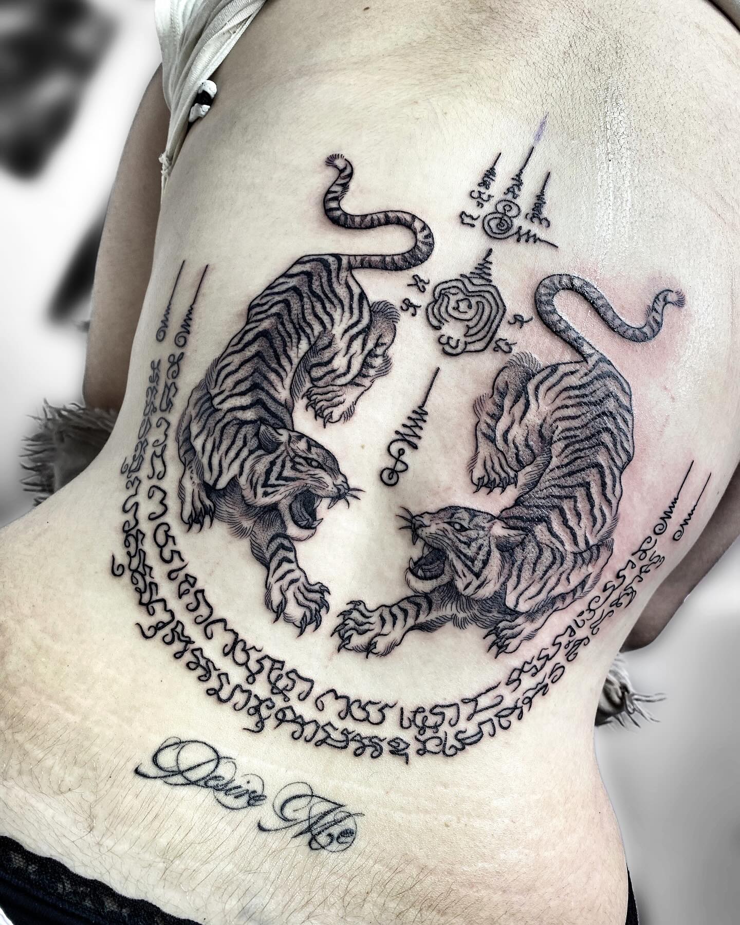 Tatuaje de dos tigres rodeados por símbolos y escritura ornamental en el torso